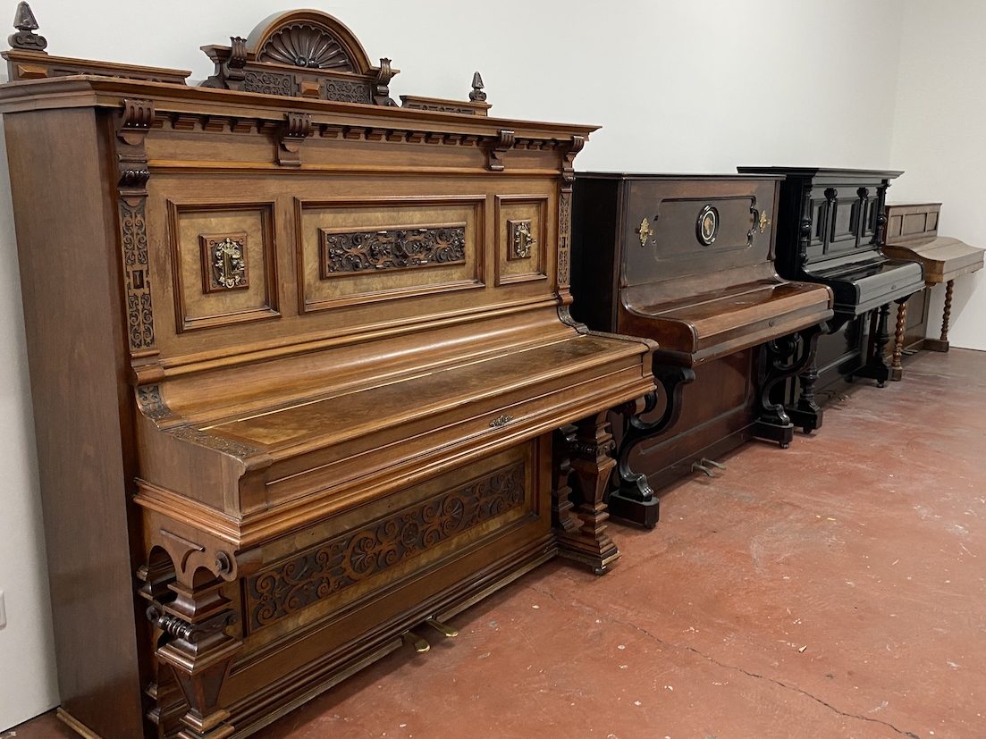 Vier historische Klaviere an weißer Wand aufgereiht